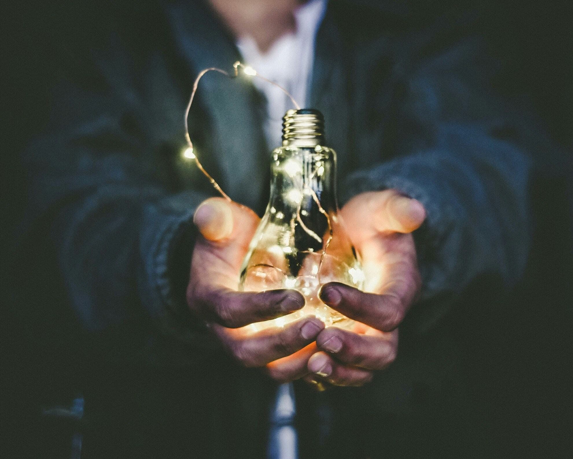 Hands holding a glowing light bulb to represent WiseWage's mission and vision